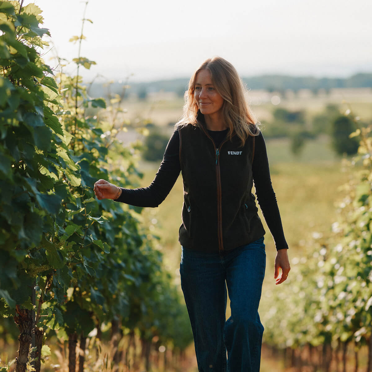 Juliane Eller, Gründerin von JUWEL Weine und Winzern, läuft durch die Weinberge in Alsheim. Sie trägt dunkelblaue Jeans und eine dunkle Fendt Weste.