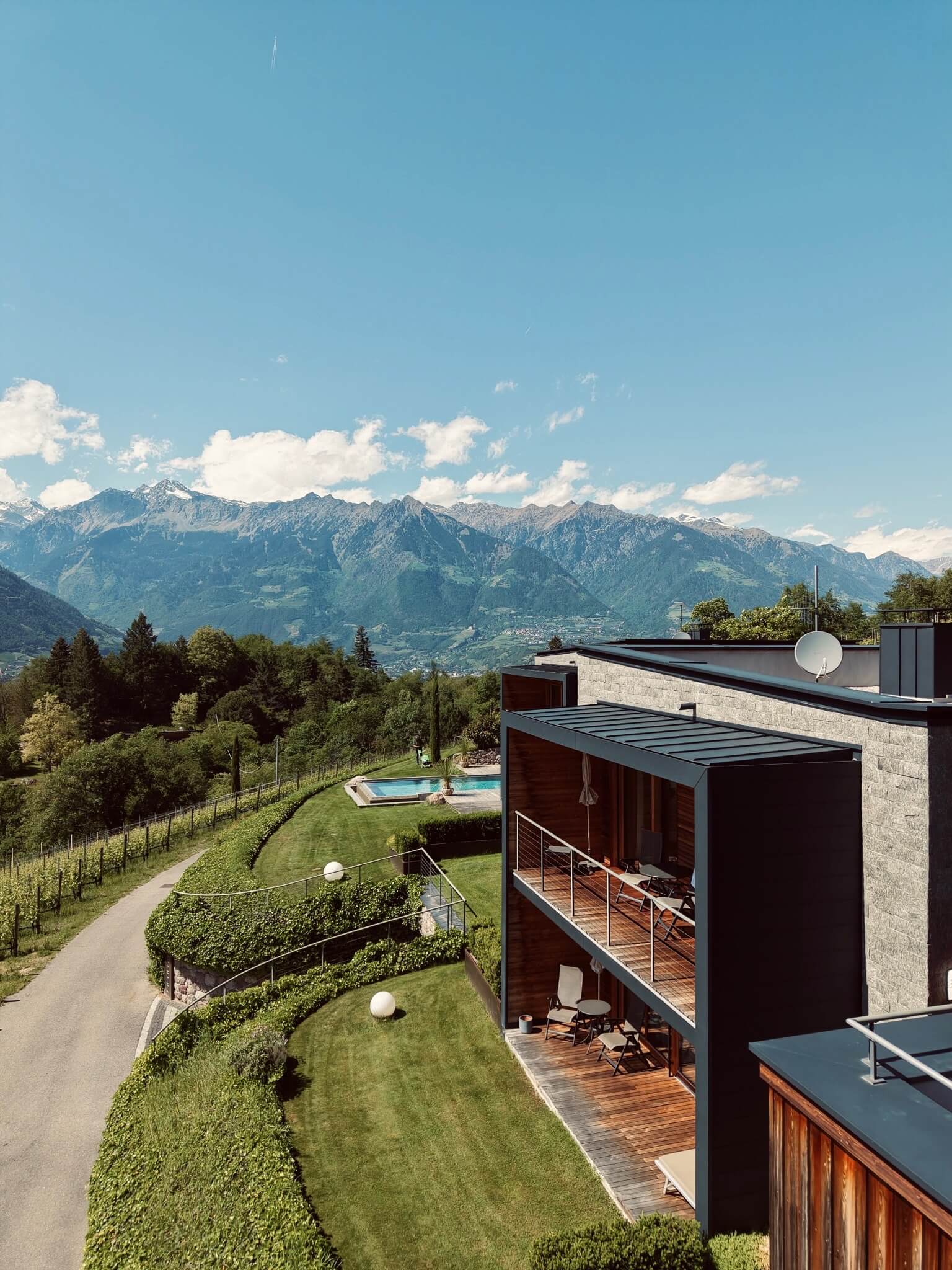 Außenansicht des Romantik Hotels Oberwirt mit Balkonen und Pool. Eingebettet zwischen grünen Bäumen, Berge im Hintergrund